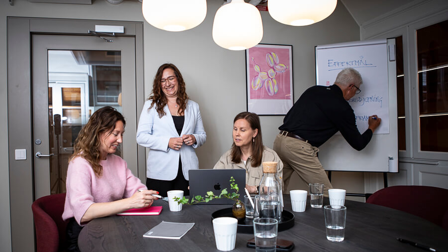 Fyra kollegor i ett mötesrum deltar i ett möte om ledarutveckling, där en man skriver på en whiteboardtavla