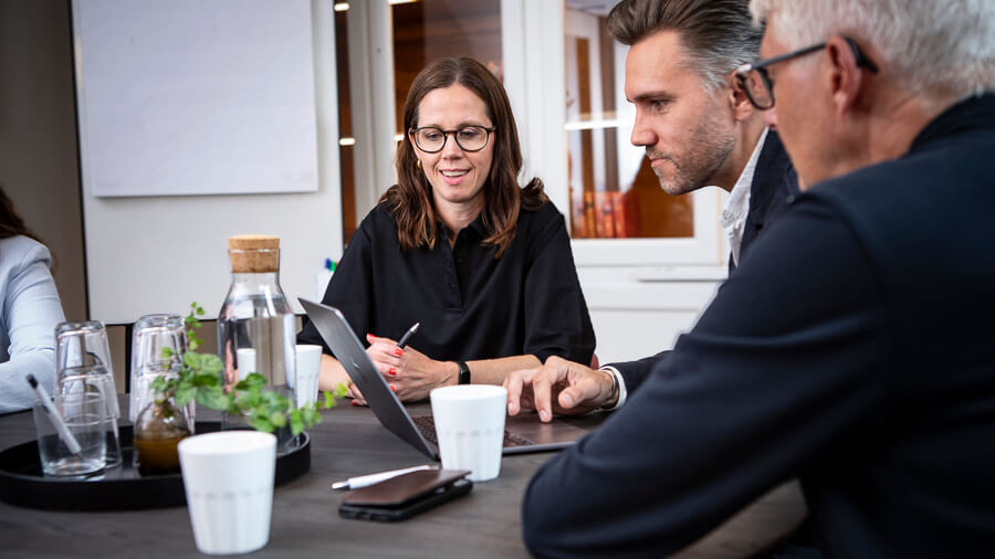 Tre personer diskuterar strategier för ledningsgruppsutveckling runt ett konferensbord